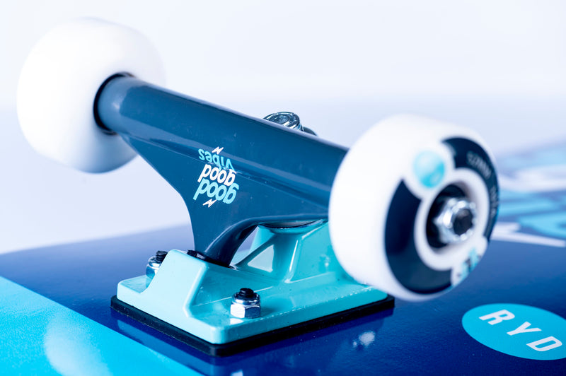 Close-up of RYD skateboard trucks and wheels on a Good Good Vibes deck, showing the hardware and branding detail