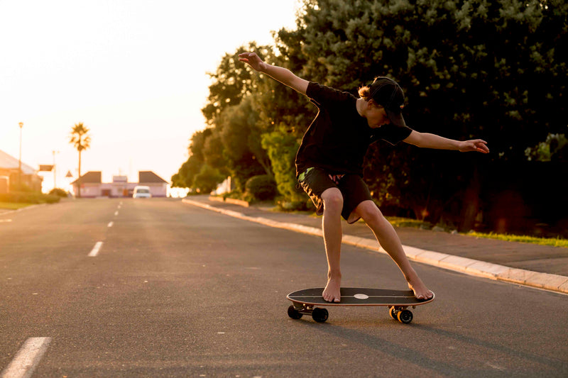 A skater carving hard on a suburban road at sunset, arms outstretched in a surf-style turn