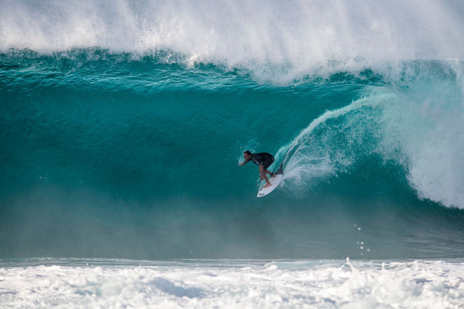 A surfer dropping down the face of a large wave, one leg kicked back to show the leash attached at the ankle