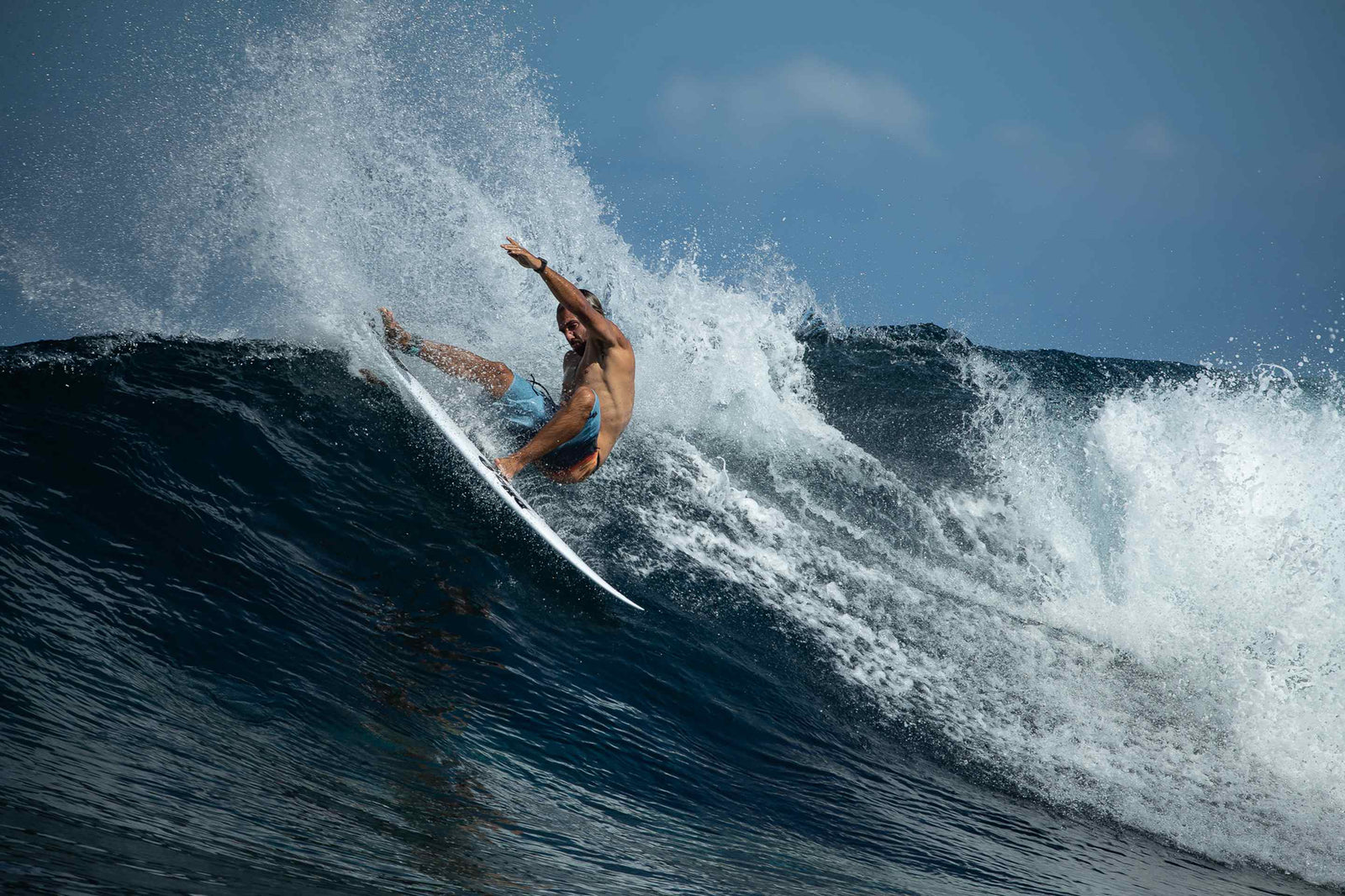 A surfer carving hard off the top of a wave, spraying a wide fan of water against a deep blue sky