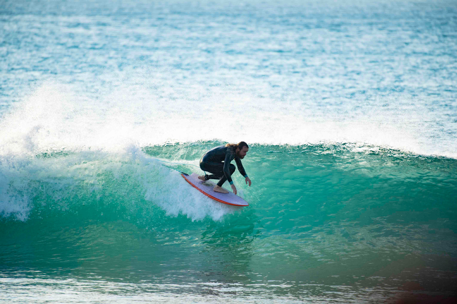 A surfer riding deep inside a large green barrelling wave, crouched low on a white surfboard trailing its leash
