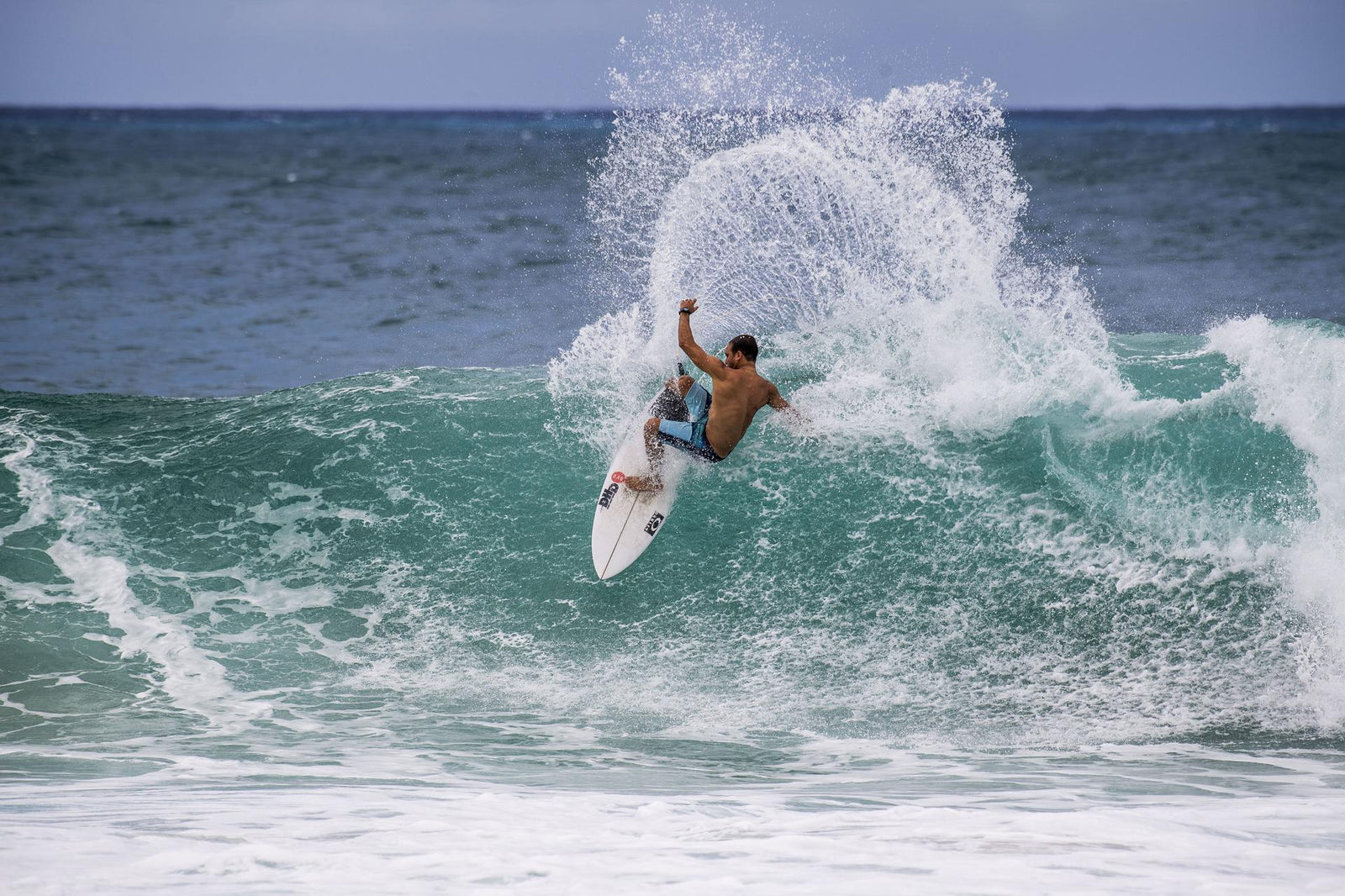 A surfer launching an aerial off the top of a wave, spraying a fan of water into the sky