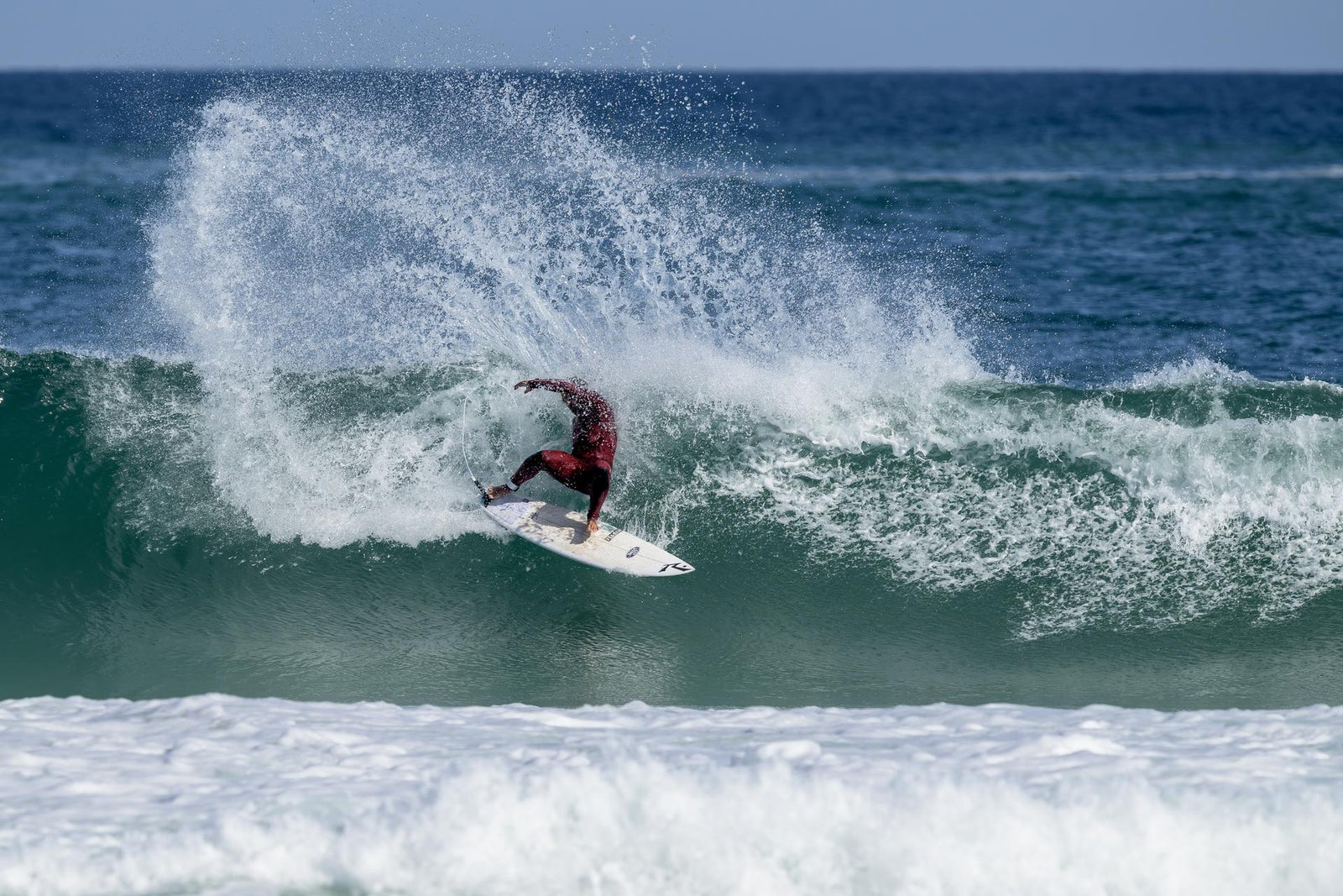 A surfer crouched low, carving along the open face of a large glassy wave