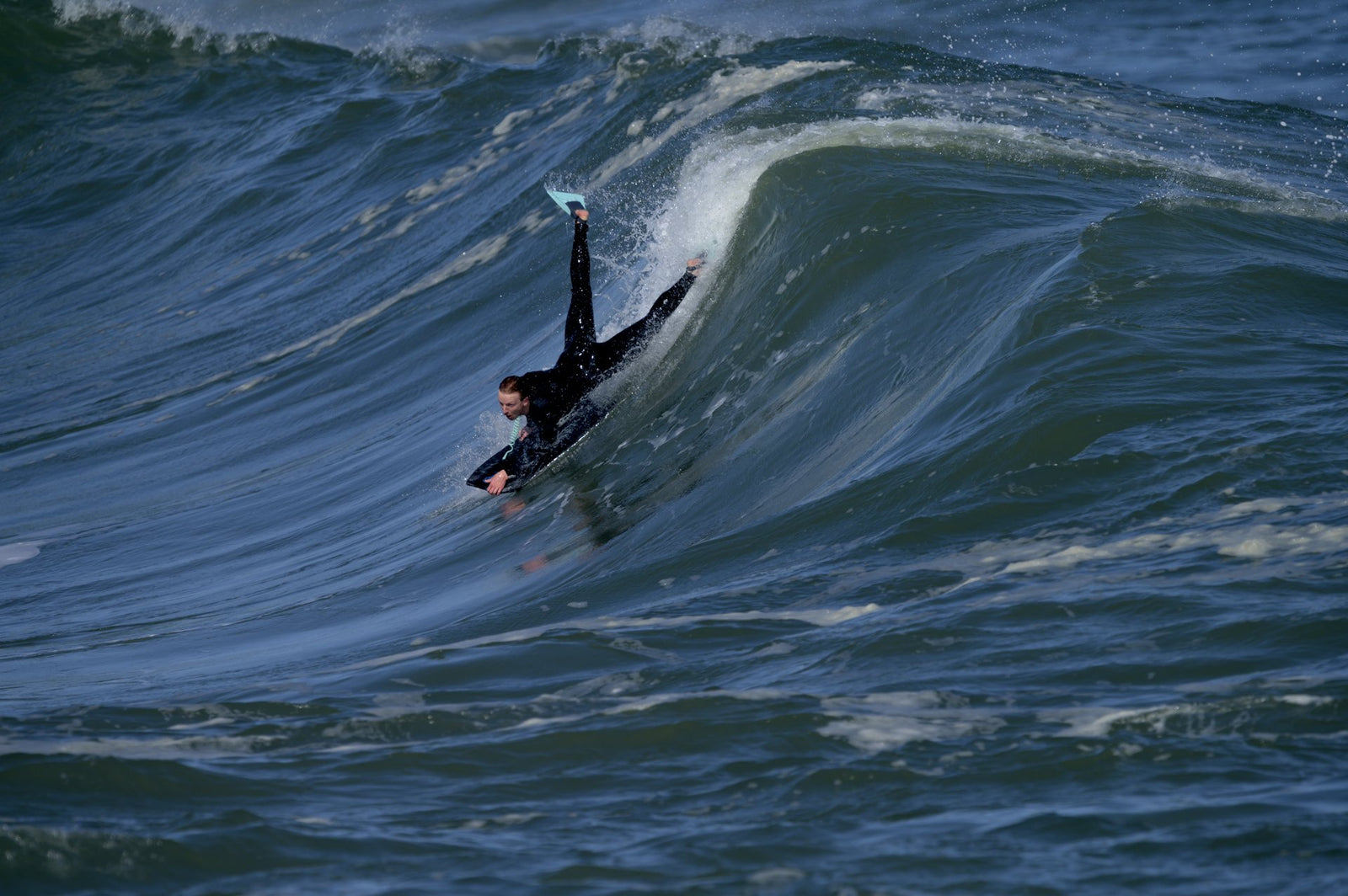 A bodyboarder wearing teal swim fins riding through the falling lip of a wave, seen from below the surface