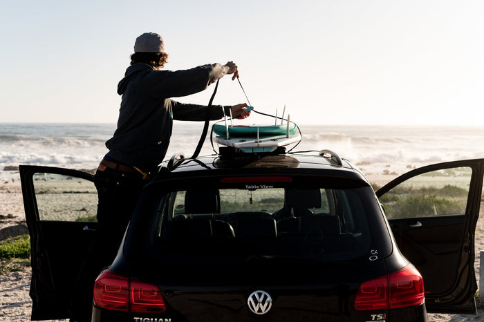Man lifting a single surfboard onto a car roof using a soft RYD travel rack pad, no roof rack bars