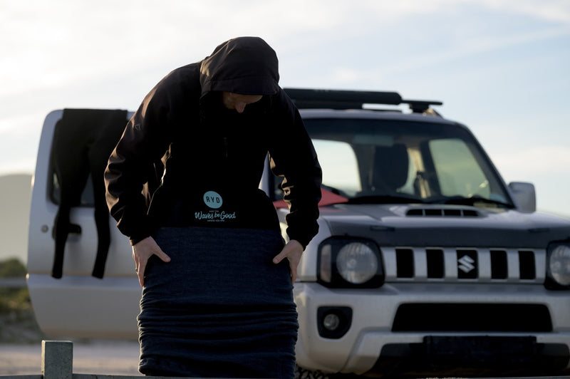 Pulling an RYD Bodyboard Range Stretch cover onto a bodyboard beside a Suzuki Jimny