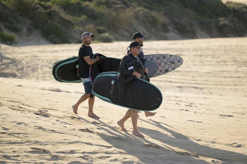 Three surfers crossing the dunes carrying RYD Alt Range board covers