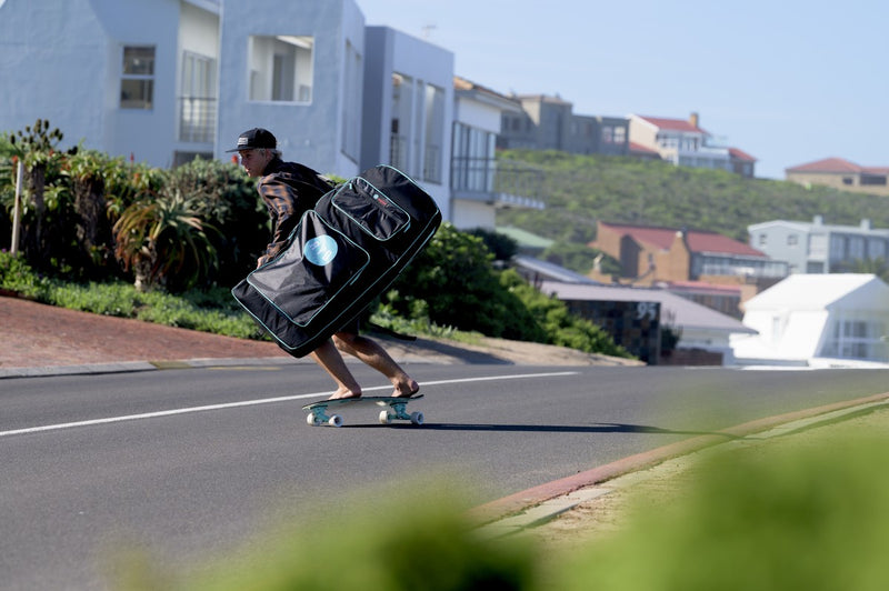 A rider skateboarding downhill while carrying an RYD Bodyboard Range board bag