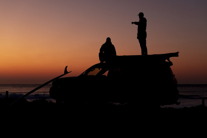 Two friends silhouetted loading RYD Layback Range board covers onto a bakkie roof rack at sunset