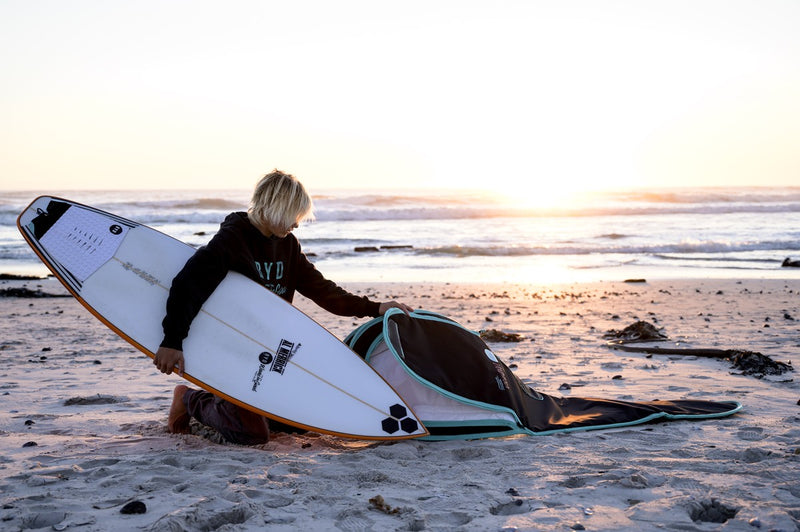 A grom packing a shortboard into an RYD True Range board cover at sunset