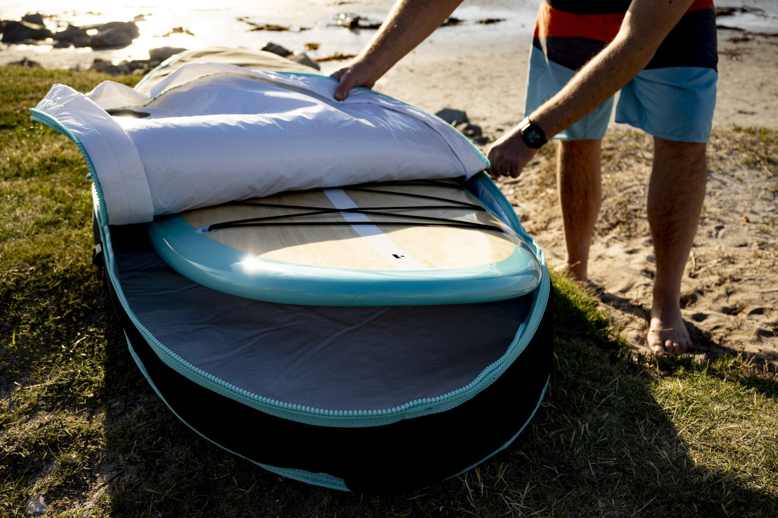 A hand unzipping an RYD SUP board cover to reveal a teal stand up paddleboard packed inside