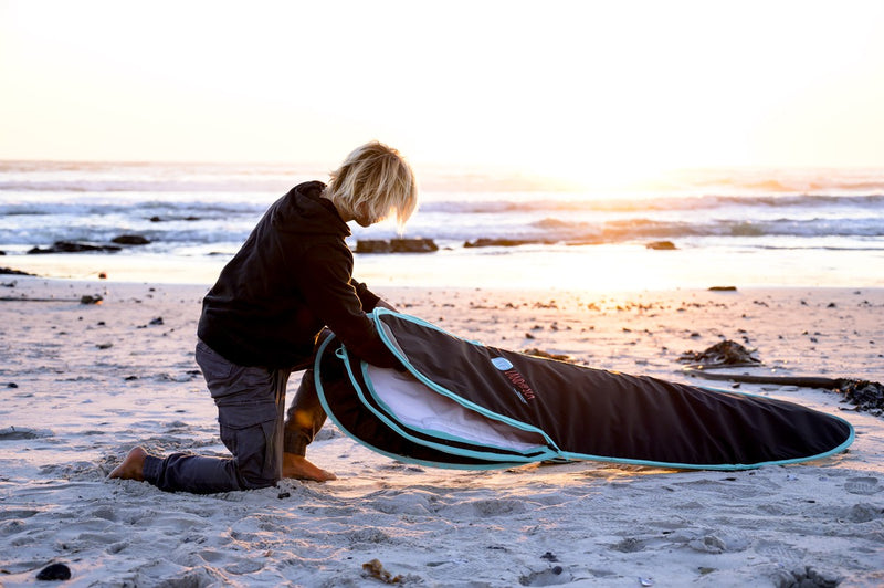 A grom zipping up an RYD True Range Everyday board cover at sunset