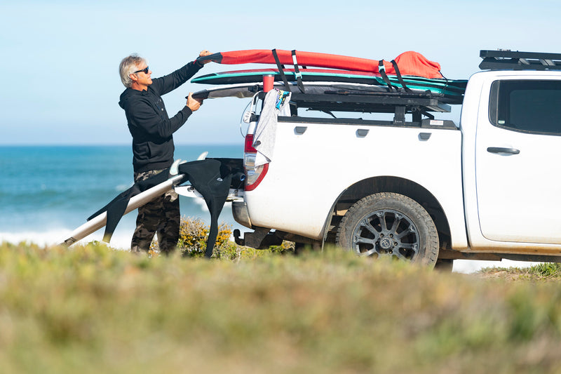 A man loading surfboards onto his 4x4's roof rack at the beach, RYD True Range Simple board cover nearby