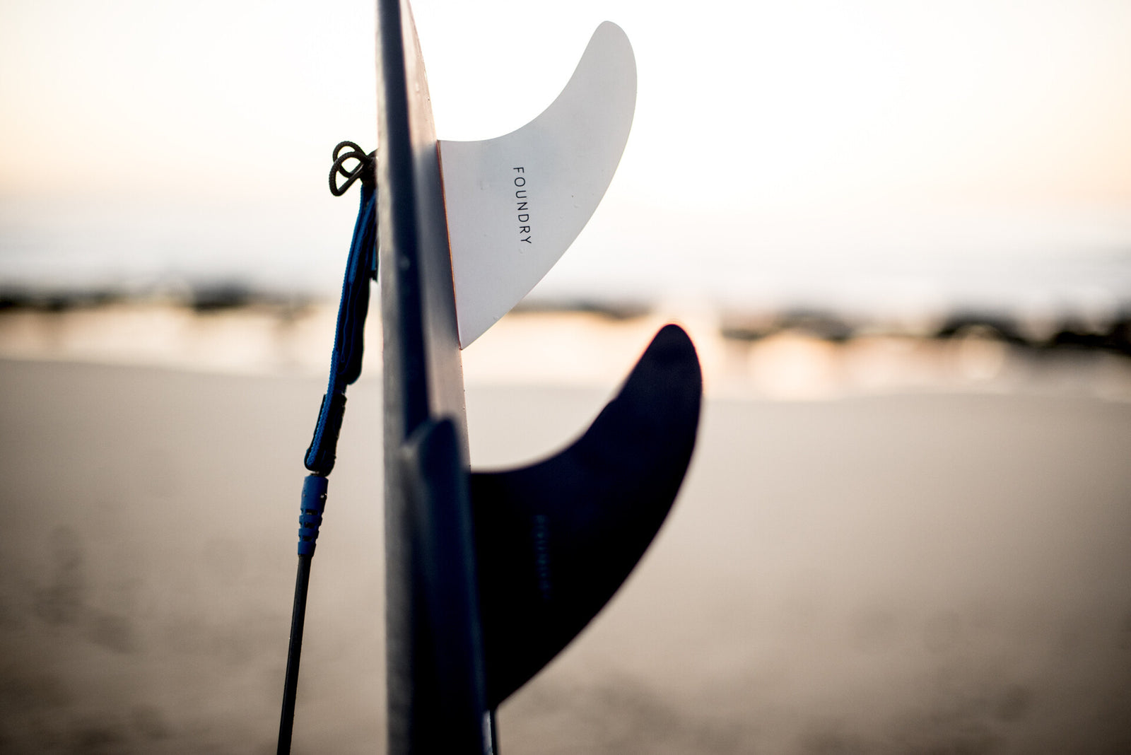 A surfer checking fins on a surfboard on the beach