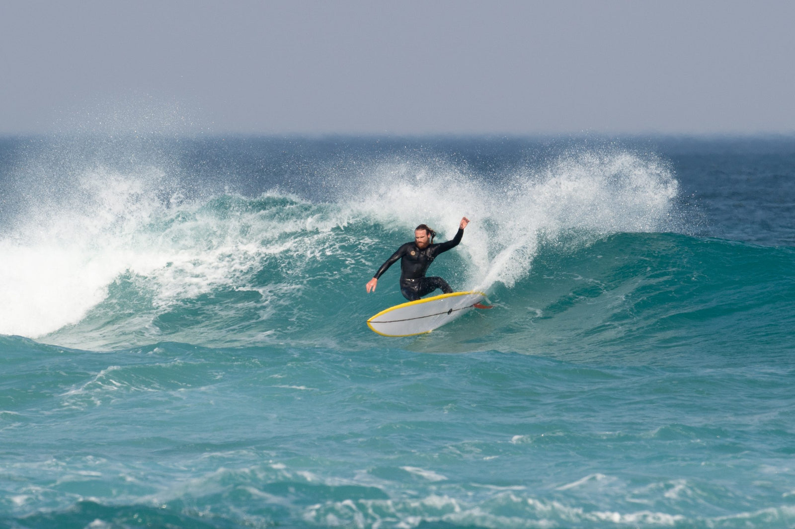 A surfer carving down the face of a wave on a longboard, one arm raised for balance