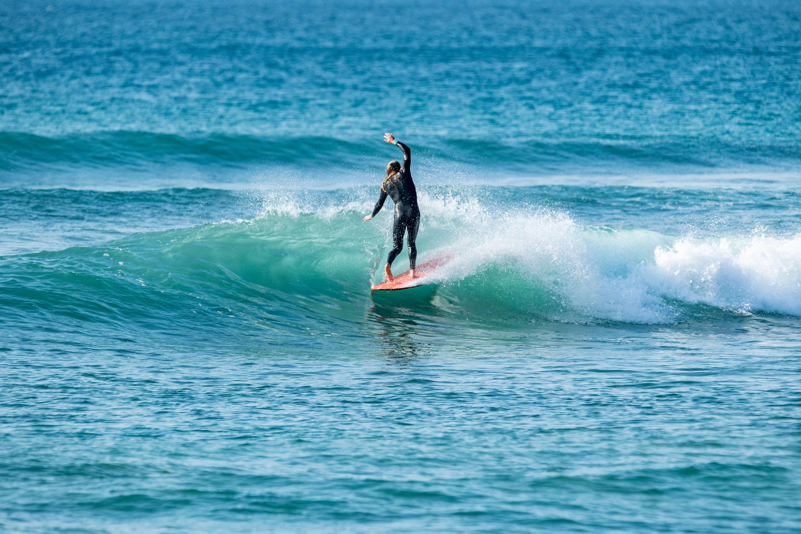 A surfer cross-stepping along a longboard with one arm raised, gliding on an open turquoise wave