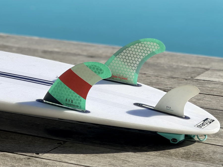 RYD Honeycomb Road Movie twin fins mounted on a surfboard, resting on a wooden deck by turquoise water