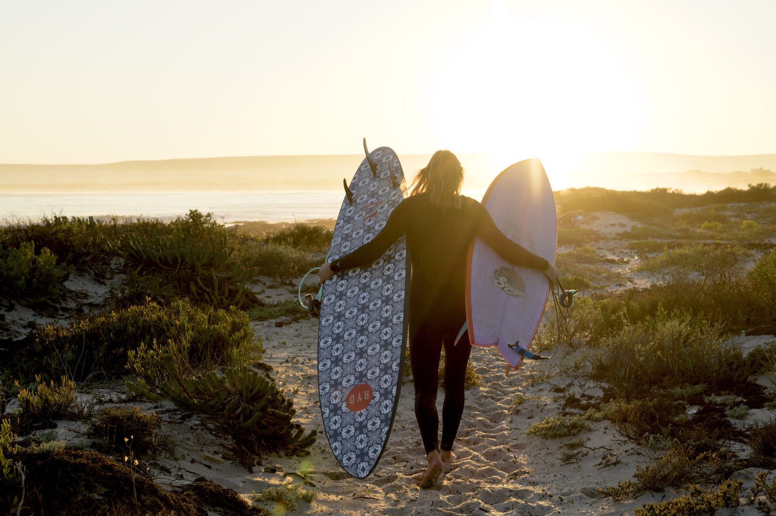 Six surfers riding the same breaking wave together on a mix of soft-top and hard surfboards, beachfront houses in the background