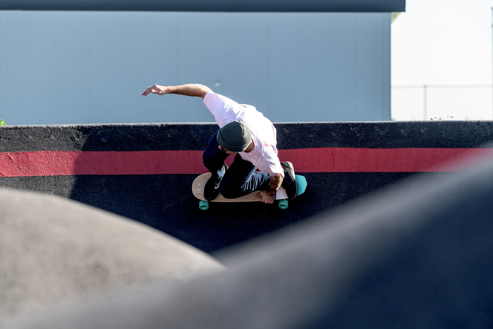 A skater carving low on a skate ramp, one hand touching down for balance, riding an RYD Everyday cruiser skateboard with turquoise wheels