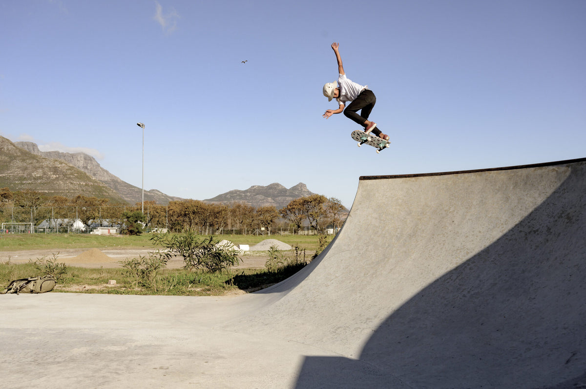 A skater airborne above a concrete bowl on an RYD street board, Cape Town mountains and open blue sky behind